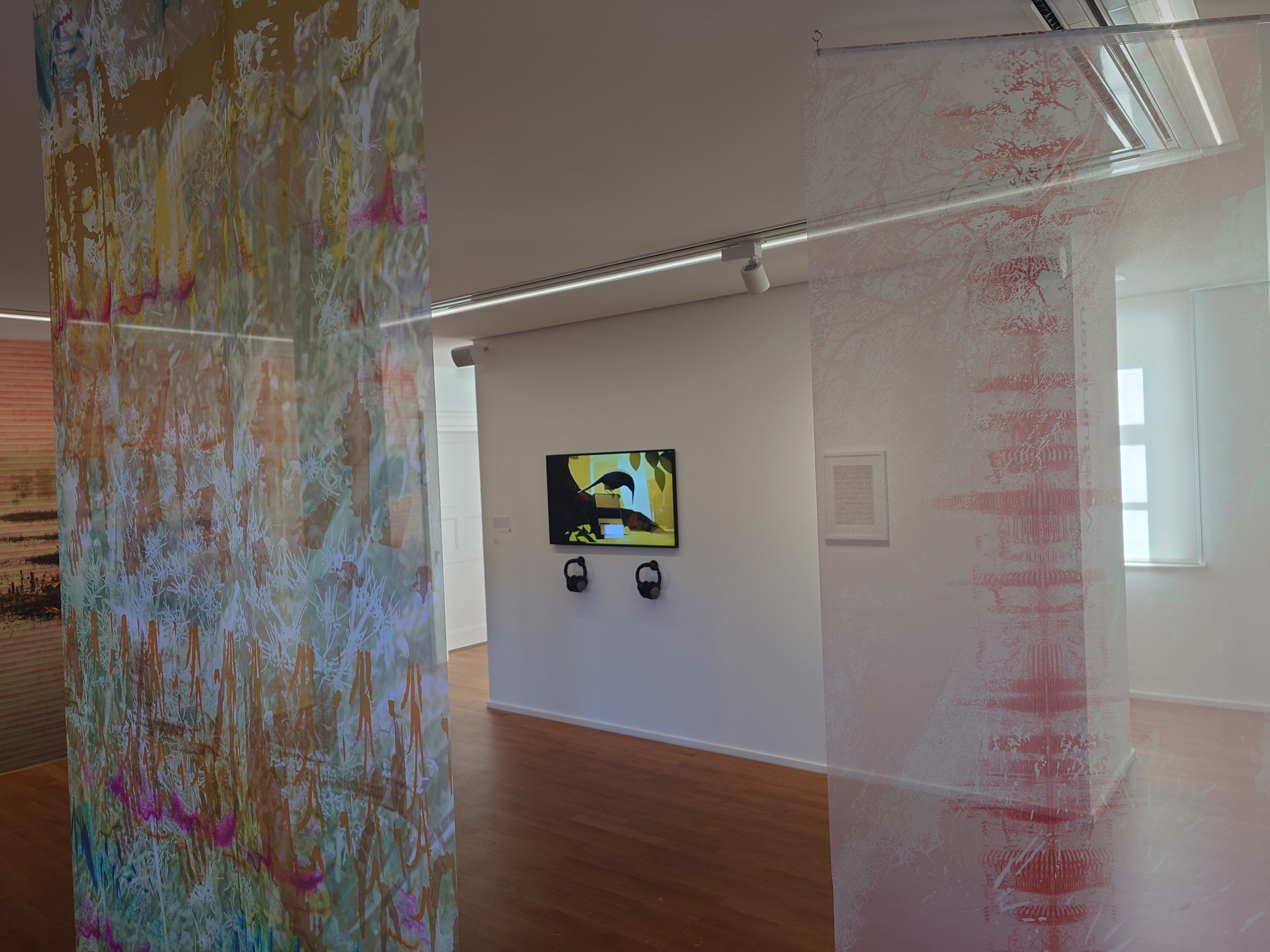 Exhibition screen with two headphones beside hanging artworks